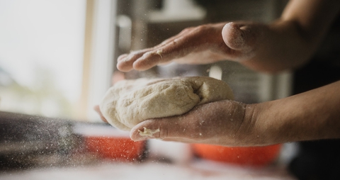 A person makes dough with the hands. You can see some particles of flour in the air.